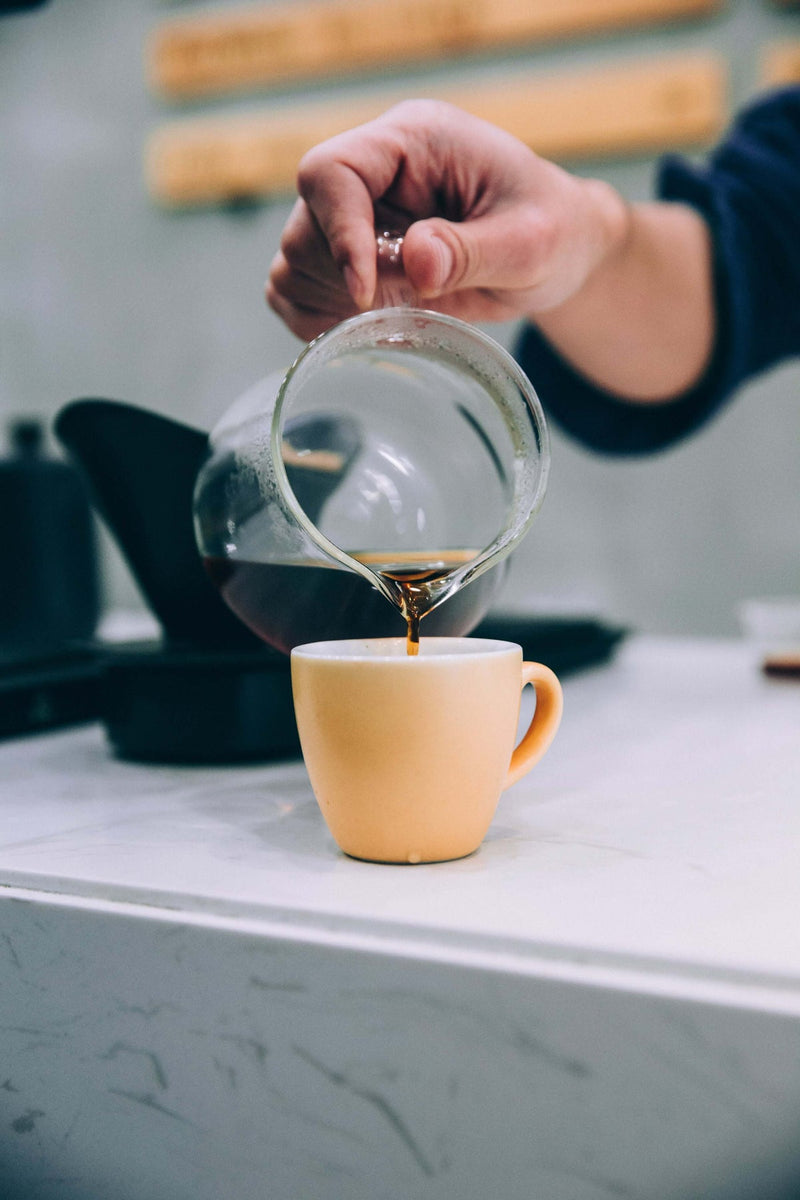 Cafea turnată dintr-o carafă de sticlă într-o ceașcă galbenă