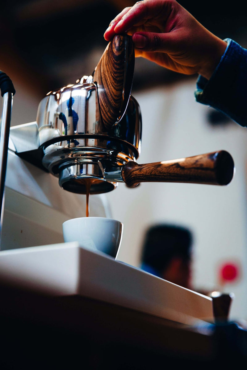 Espresso în curs de extracție dintr-un portafiltru, curgând într-o ceașcă albă