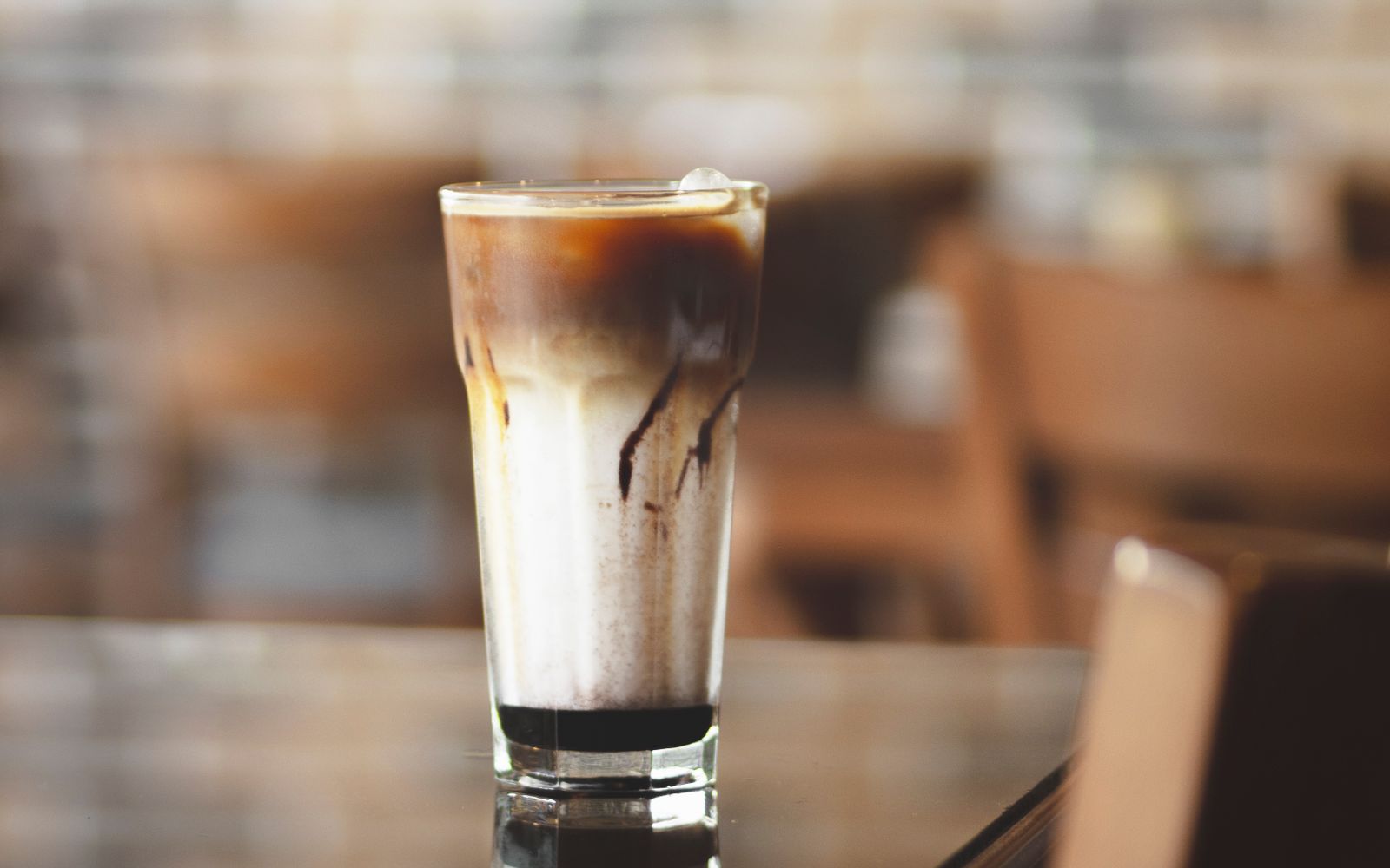 Pahar înalt cu cafea rece și cuburi de gheață, pe o masă de cafenea