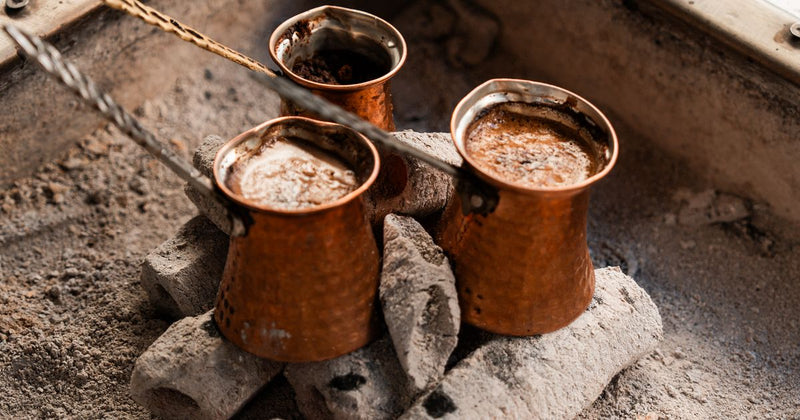 Trei ibrice de cupru cu cafea fierbând pe jar și nisip încins, în stil tradițional turcesc