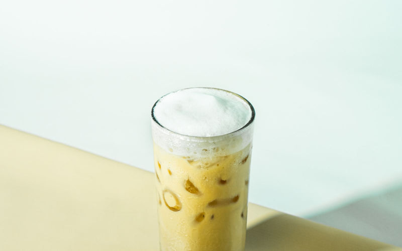 Pahar înalt de cafea rece cu strat gros de spumă albă de lapte deasupra, în stilul unui freddo cappuccino
