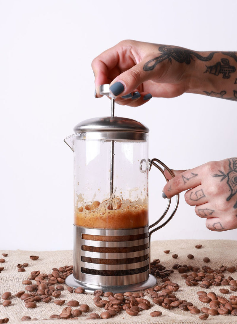 French Press din sticlă cu cafea proaspăt infuzată și boabe de cafea pe masă