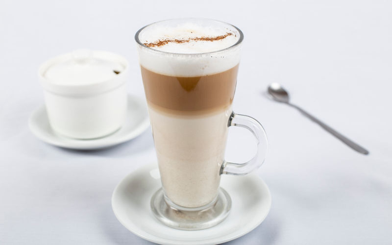 Latte macchiato stratificat în pahar înalt: lapte jos, espresso la mijloc, spumă deasupra