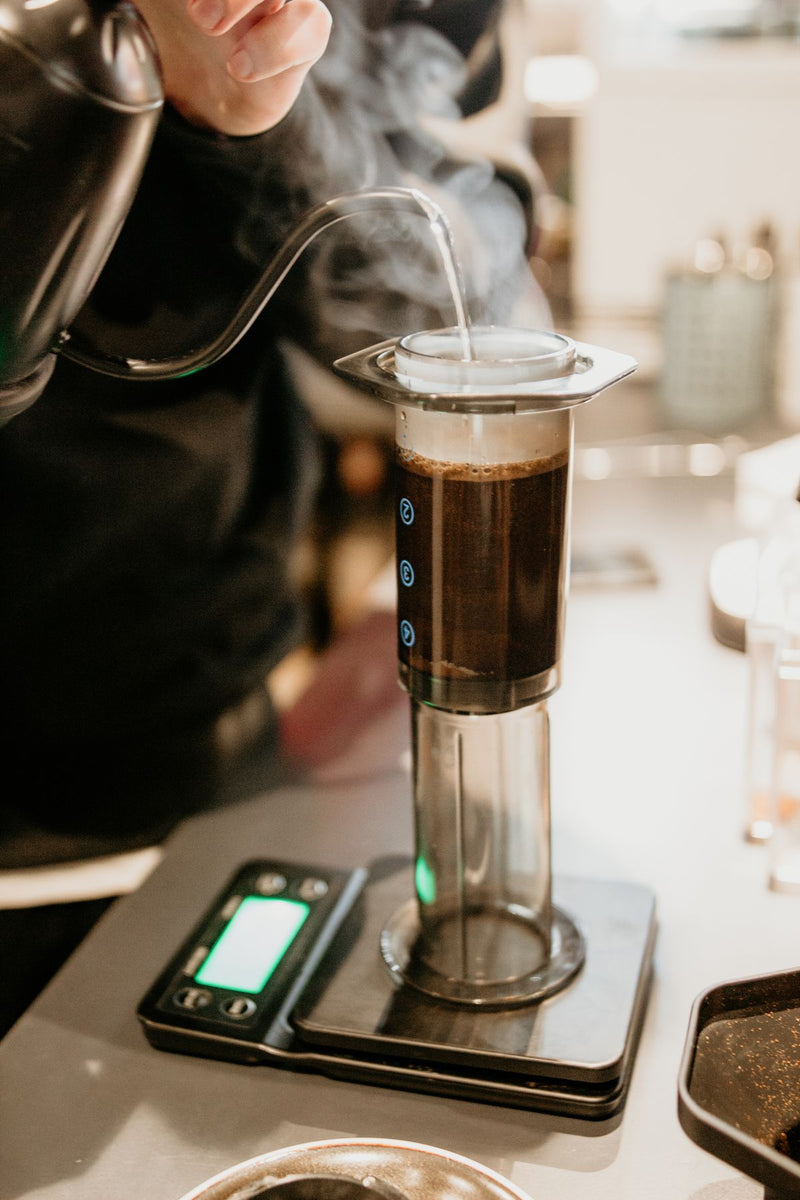Barista toarnă apă fierbinte dintr-un ibric cu gât de gâscă într-un AeroPress pe cântar