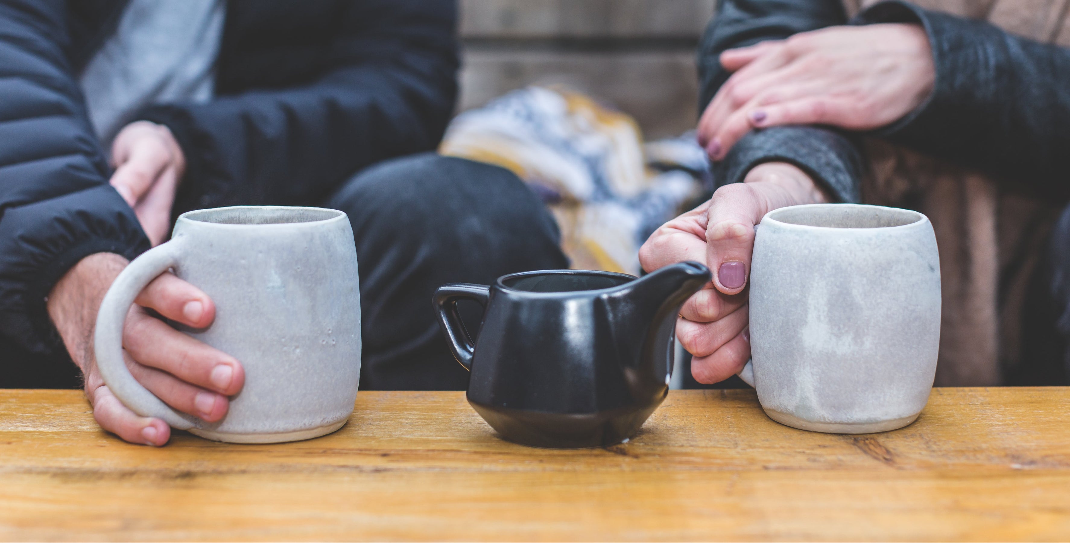 doi oameni care stau la masa cu cana de cafea in mana